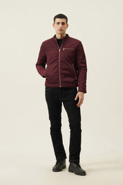 Man wearing a burgundy jacket and black pants on a beige background